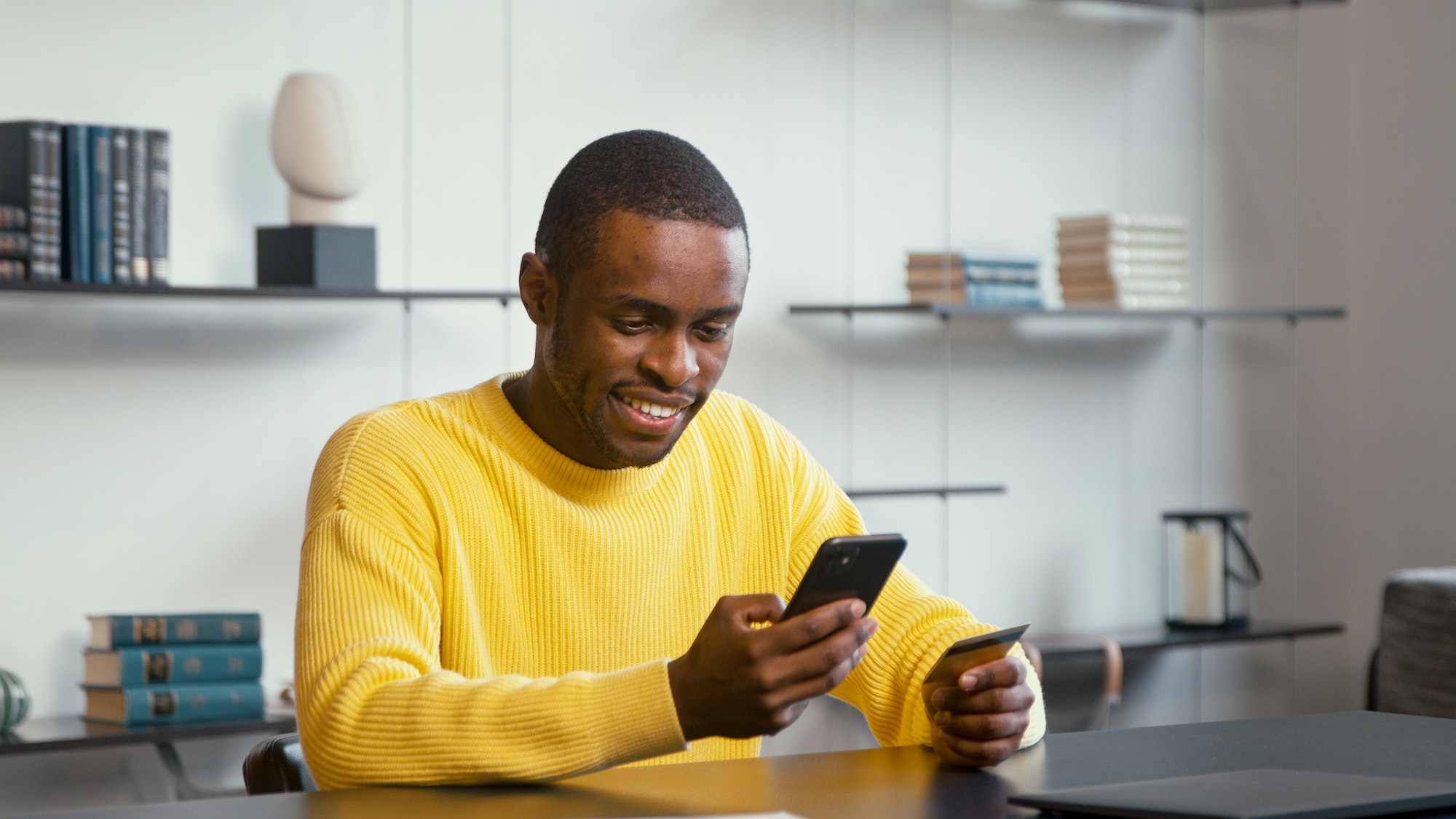 Smiling financial director in yellow shirt looks at bank card in hand