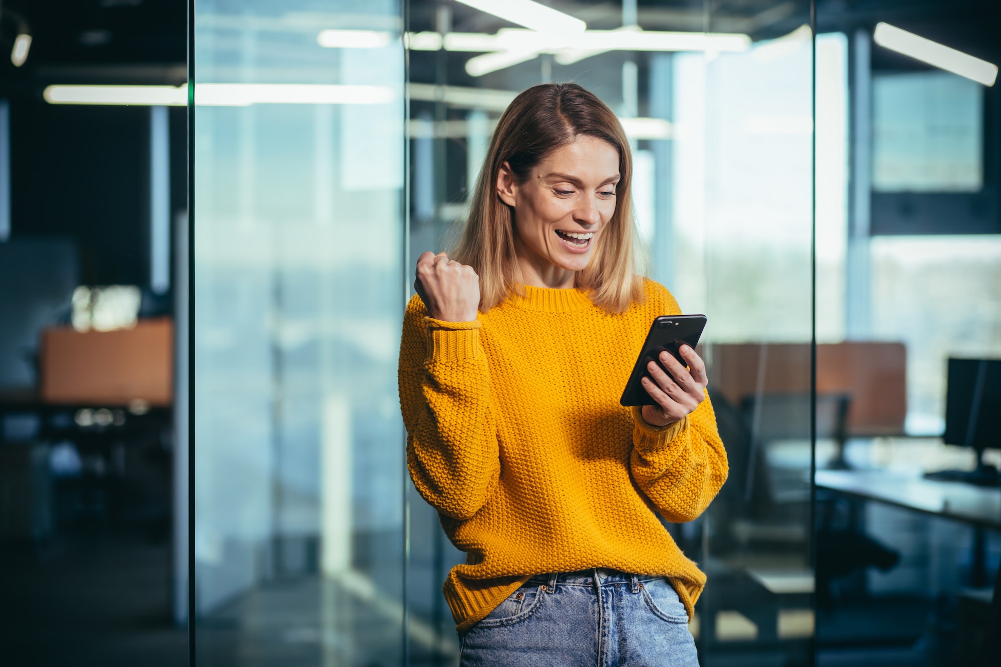 Successful freelancer woman using phone rejoices in winning success, looks at phone