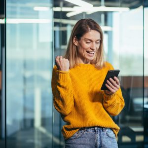 Successful freelancer woman using phone rejoices in winning success, looks at phone